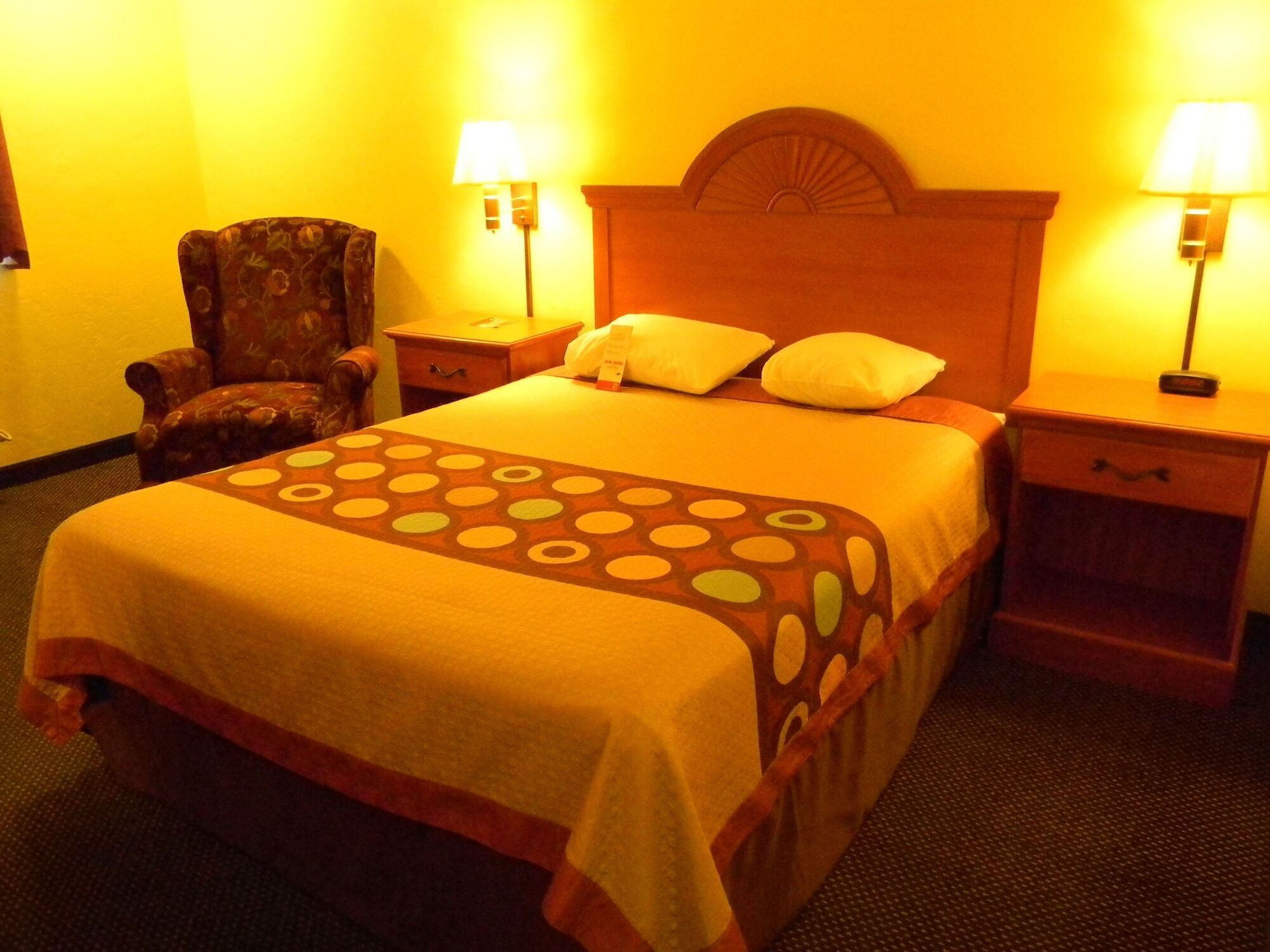 Una habitación de hotel con una cama, dos mesitas de noche, una silla y dos lámparas.