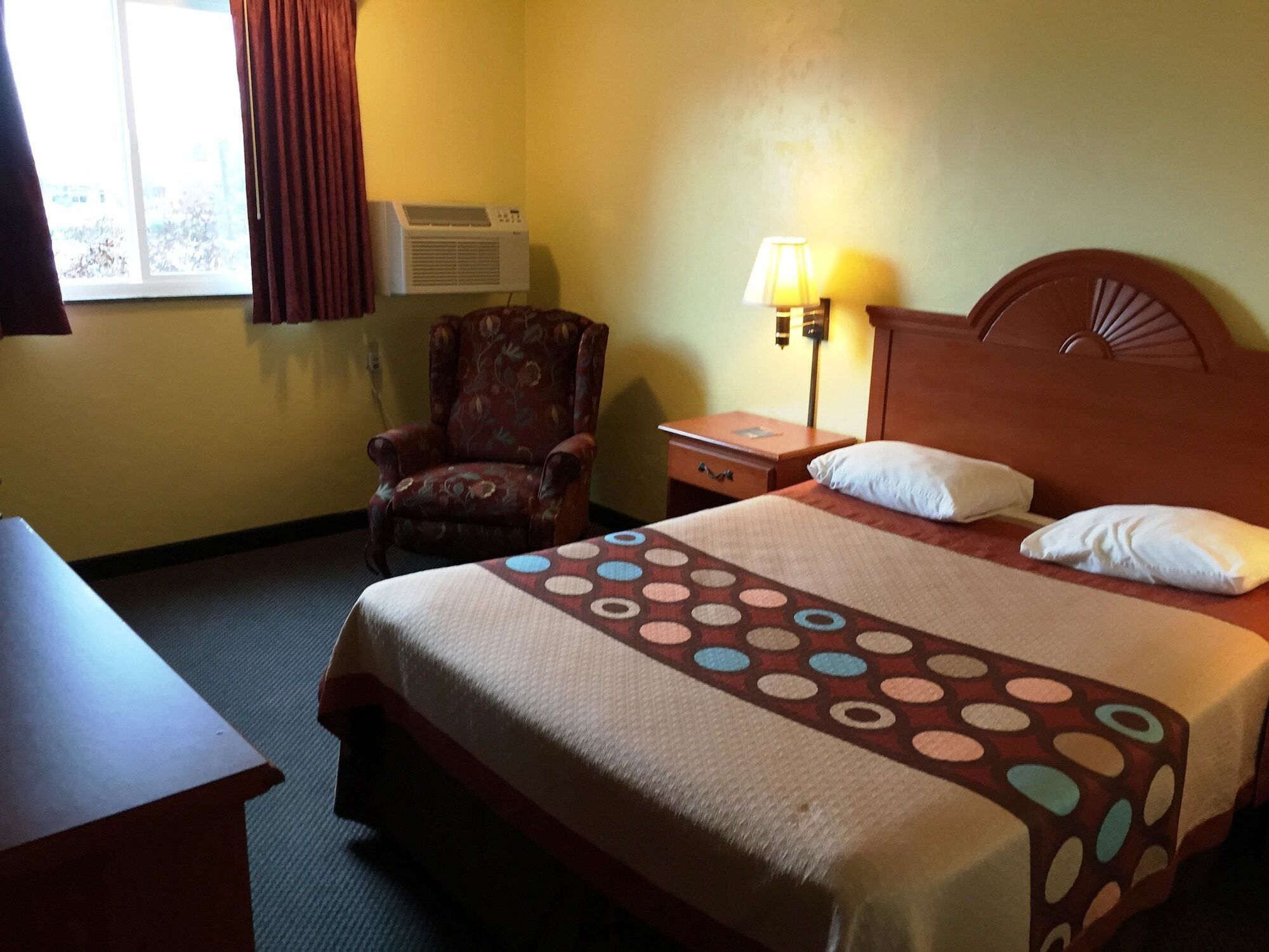 A hotel room with a bed, a chair, a desk, and a lamp.