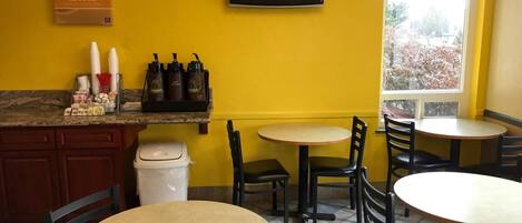Un interior de restaurante con paredes amarillas, un televisor de pantalla plana y varias mesas y sillas.