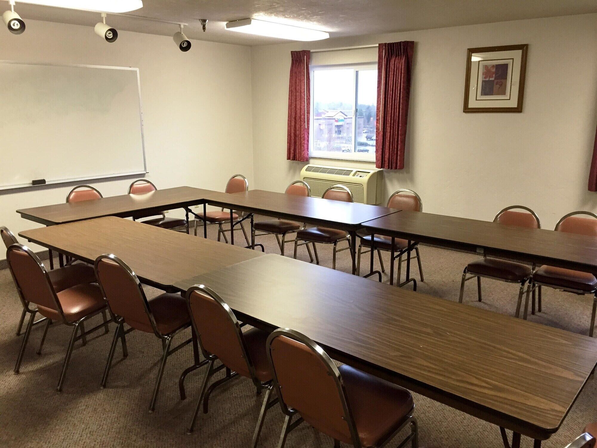 A conference room with a long table, chairs, a whiteboard, and a window with curtains.
