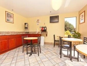 A kitchen with a marble countertop, wooden cabinets, and a tiled floor. There are two dining tables with chairs. - Motel 6 Wilsonville, OR - Portland (Wilsonville)