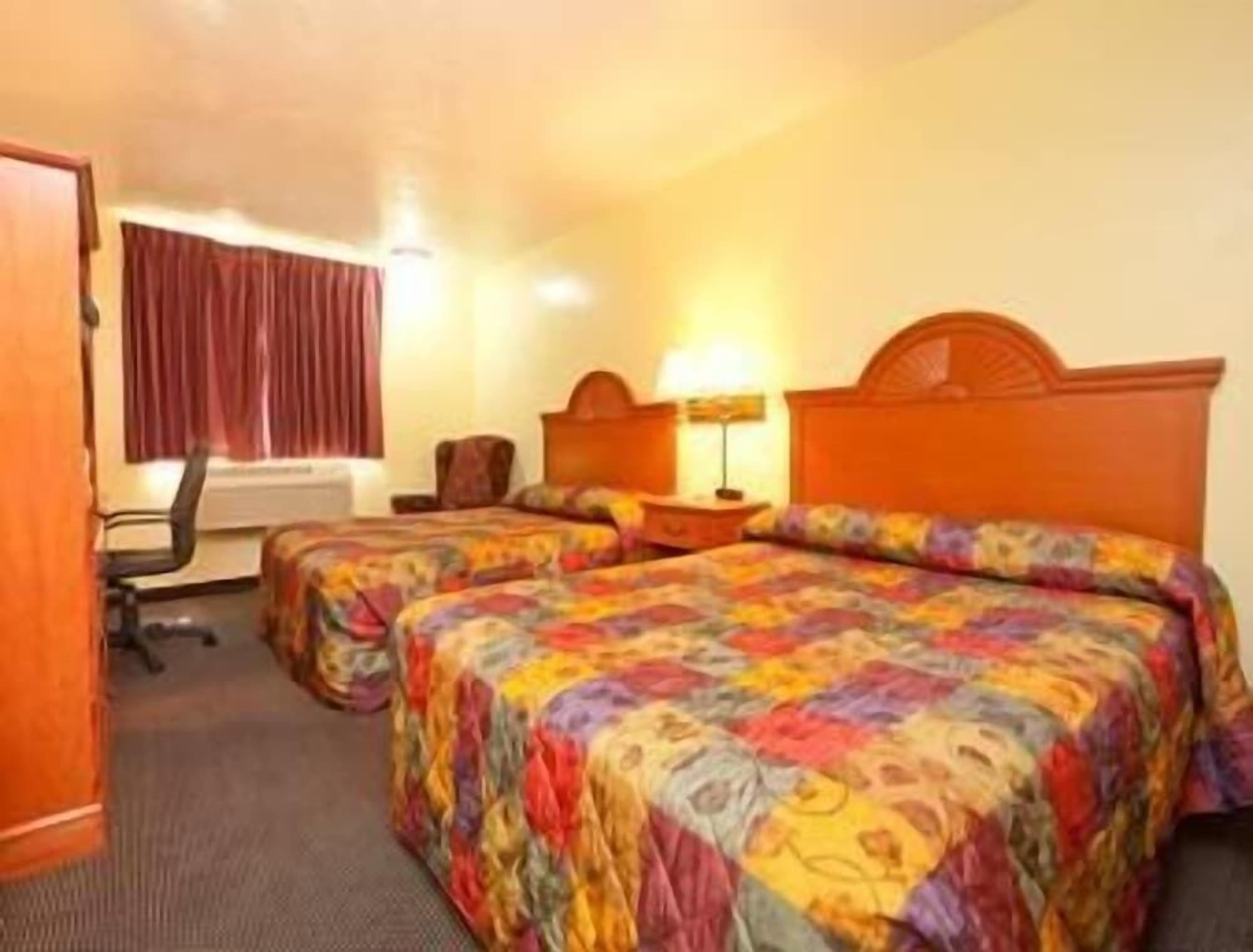 Une chambre d’hôtel avec deux lits, un bureau, une chaise et une fenêtre avec des rideaux.
