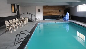 En indendørs swimmingpool med krystalklart vand, omgivet af hvide stole og et lille bord.