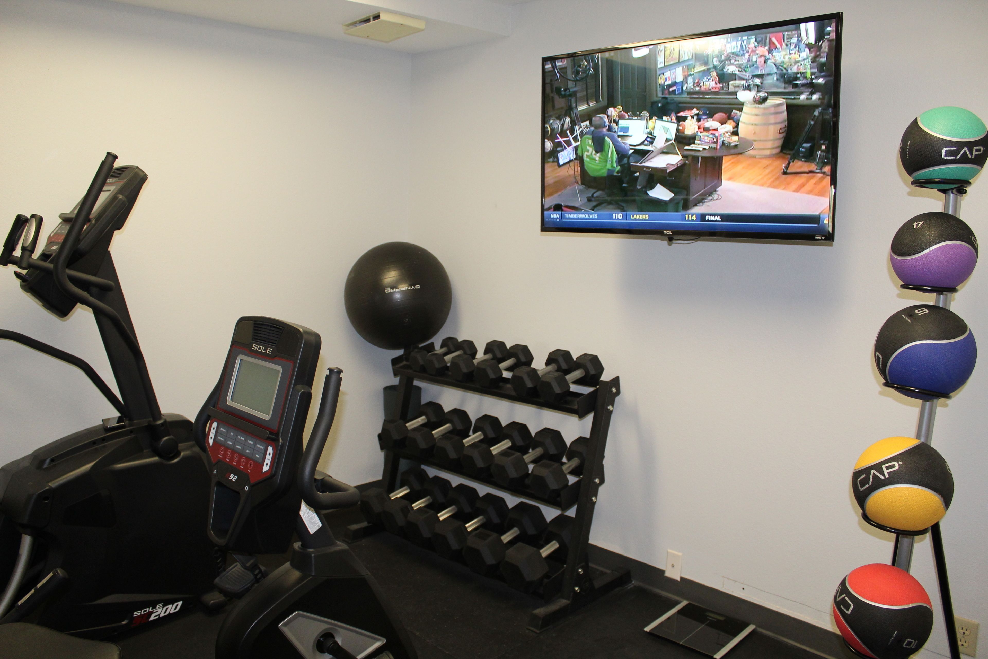 A home gym with a treadmill, dumbbells, and exercise balls.