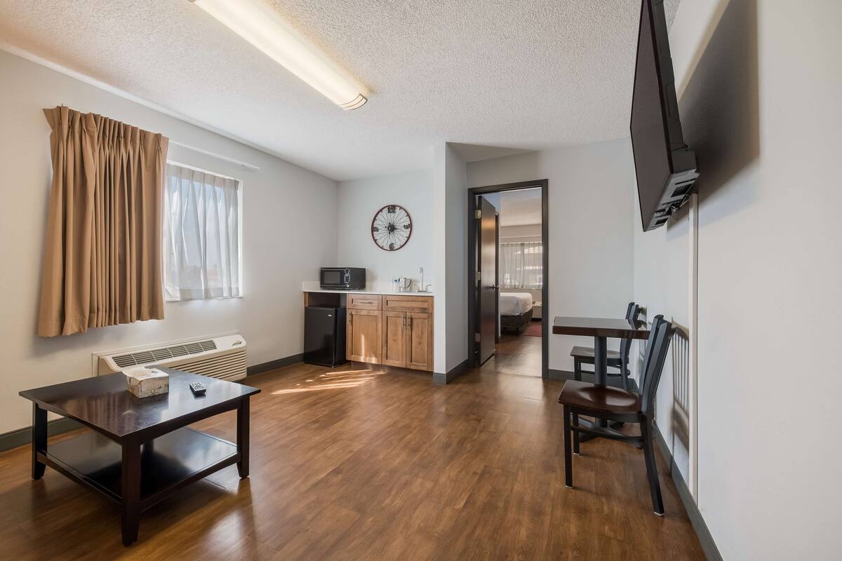 A modern living room with a dark wooden table, a kitchen area with a microwave, and a dining area with a chair.