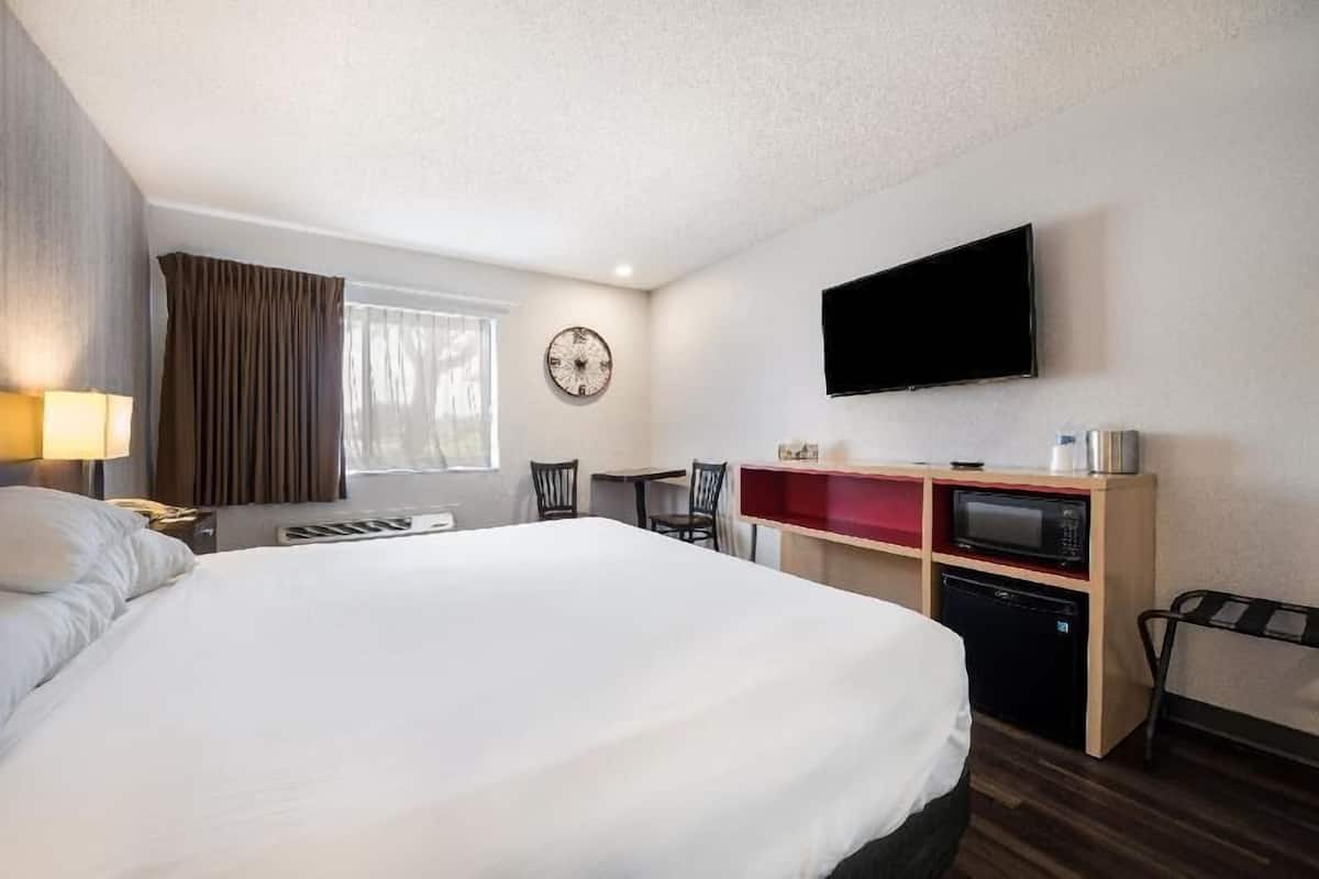 A hotel room with a bed, a desk with a lamp, a TV, a clock, and a microwave.