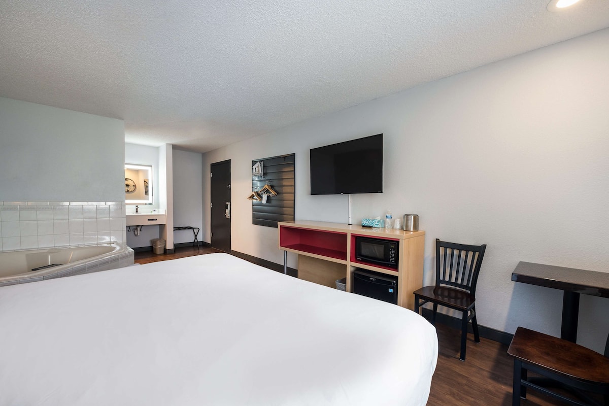 A hotel room with a large bed, a flat-screen TV mounted on the wall, a microwave, and a small table.