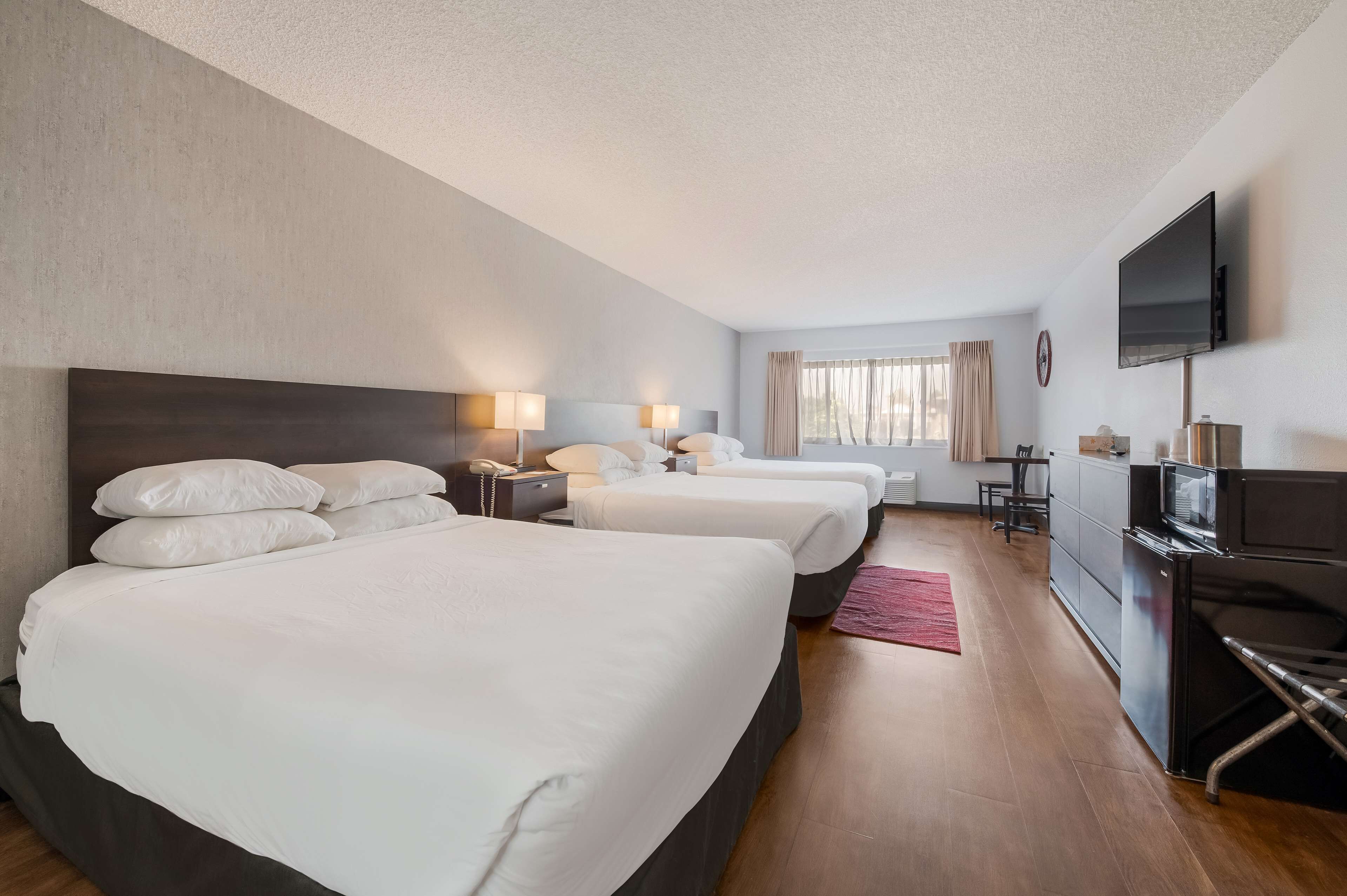 Une chambre d’hôtel avec trois lits, une télévision, un bureau et une fenêtre avec des rideaux.