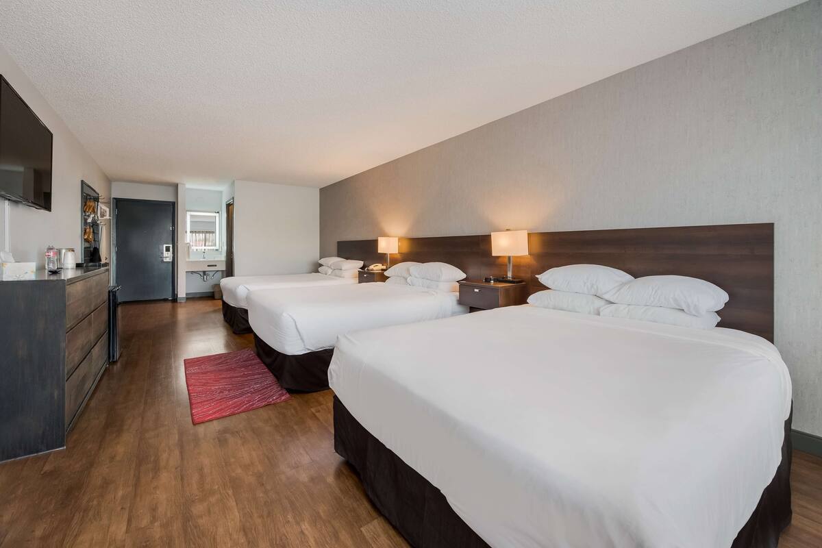 A hotel room with two single beds, a desk with a chair, a TV, and a small kitchenette.
