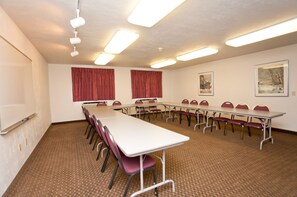 Un salón de conferencias con una larga mesa, sillas, cortinas rojas, cuadros en la pared y luces en el techo.