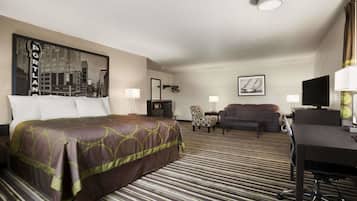 Quarto de hotel com cama, escrivaninha, cadeira, sofá e televisão.