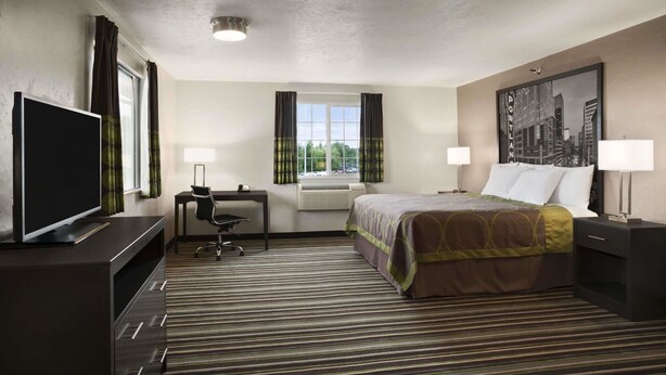 Habitación de hotel con cama, escritorio, silla, televisión y ventana con cortinas.