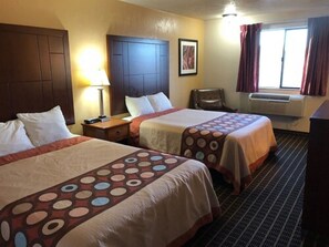 Ein Hotelzimmer mit zwei Betten, einem Schreibtisch, einem Stuhl, einem Fenster mit Vorhängen und einer Klimaanlage.