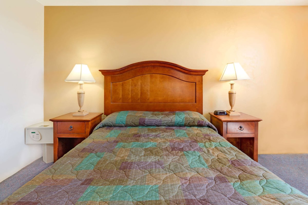 A neatly made bed with a quilt, two bedside tables with lamps, and a nightstand with a clock.