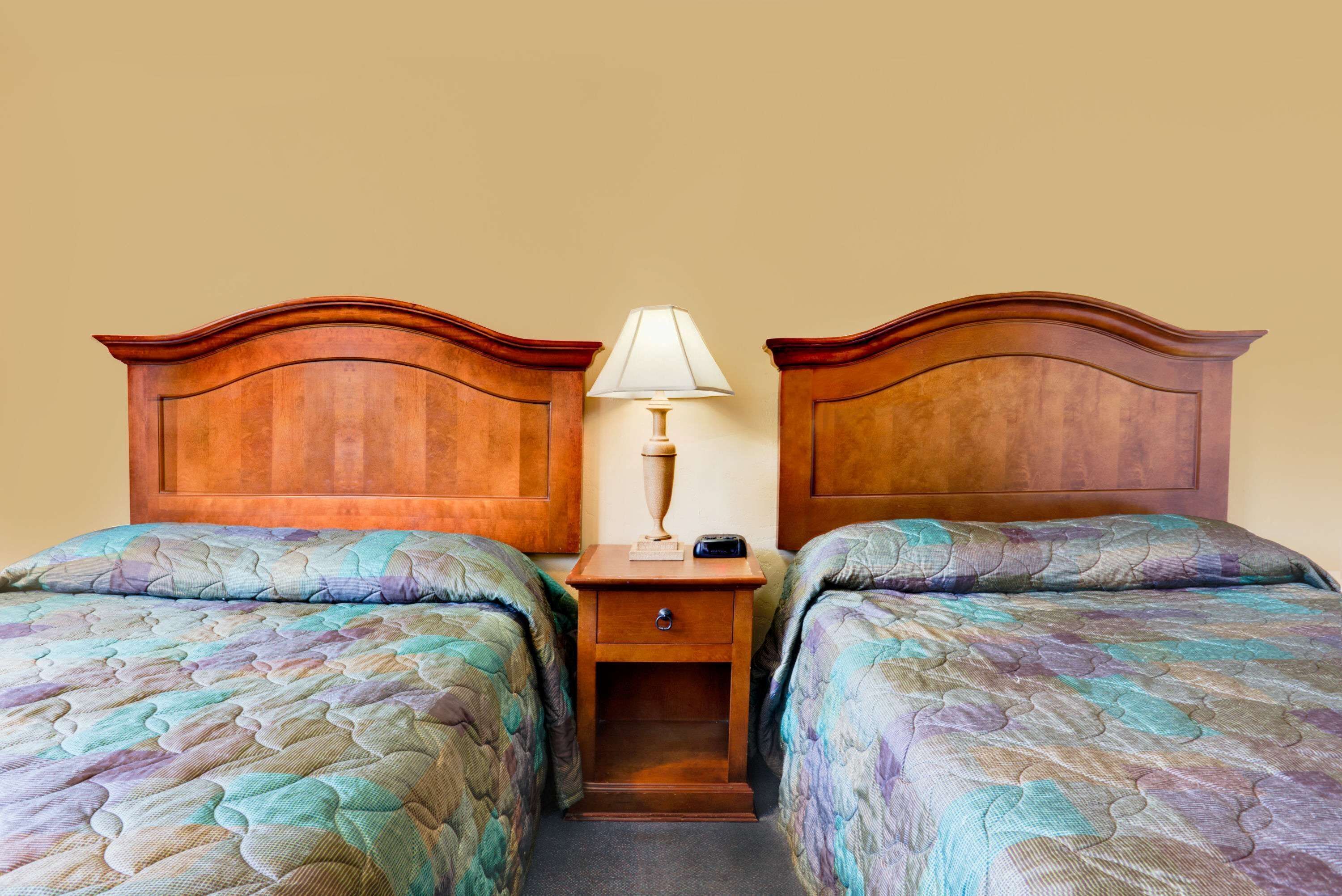 A double room with two wooden headboards, a bedside table with a lamp, and a bed with a patterned quilt.