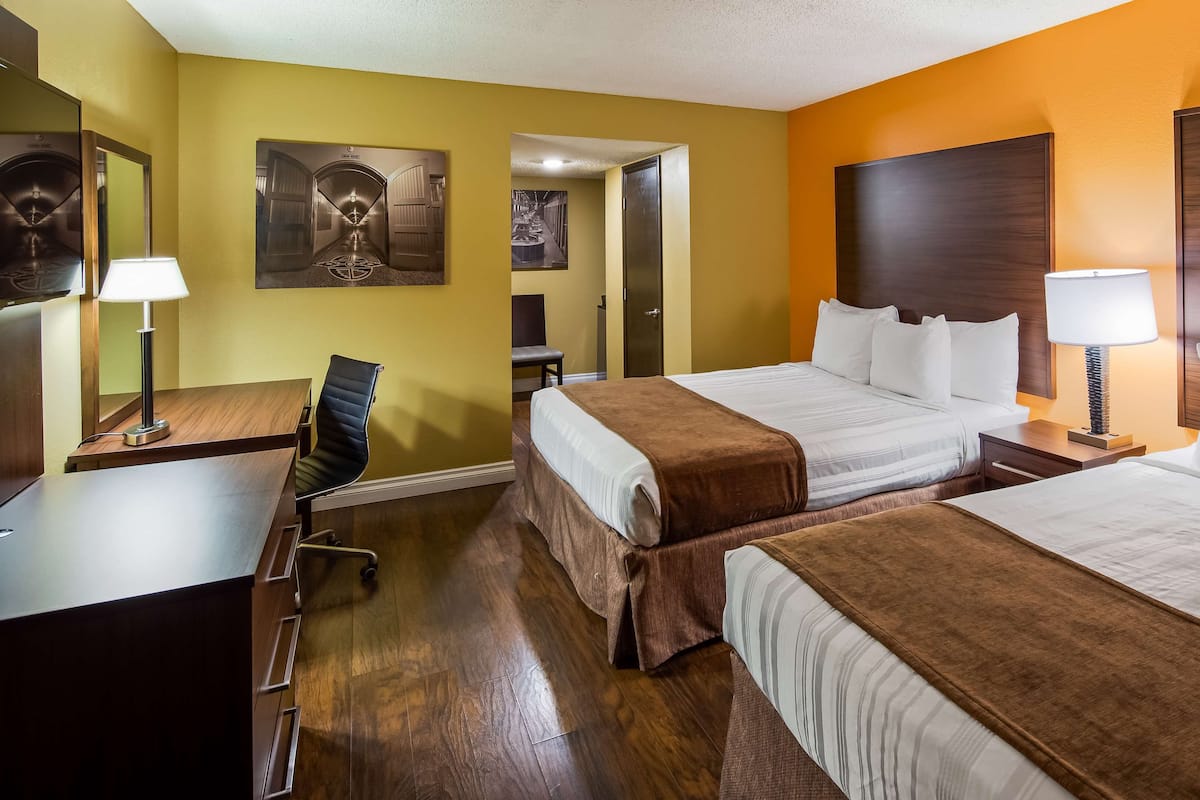 Une chambre d’hôtel avec deux lits, un bureau, une chaise, une lampe et un tableau au mur.