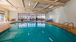 Una piscina interior con agua cristalina, rodeada de sillones y mesas, con grandes ventanales que ofrecen vistas al exterior.