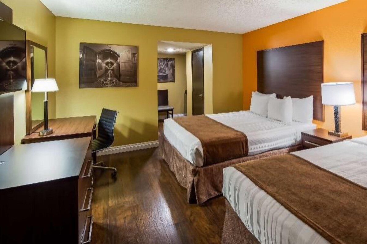 A hotel room with two beds, a desk, a chair, and a door leading to another room.