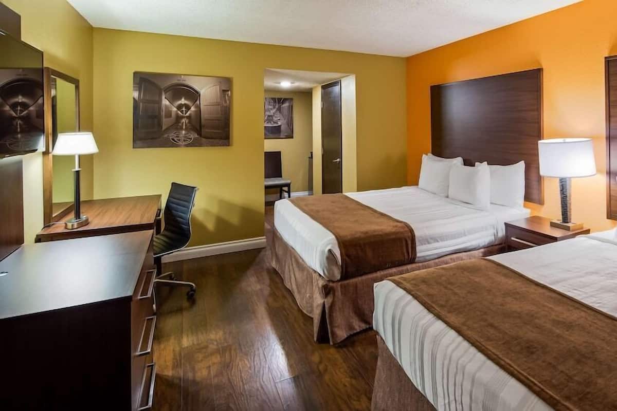 Une chambre d’hôtel avec deux lits, un bureau, une chaise et une table de chevet avec une lampe.