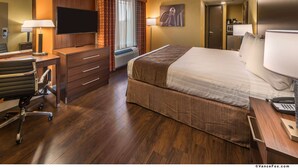 Habitación de hotel con una cama grande, un escritorio con silla, televisor y ventana con cortinas.