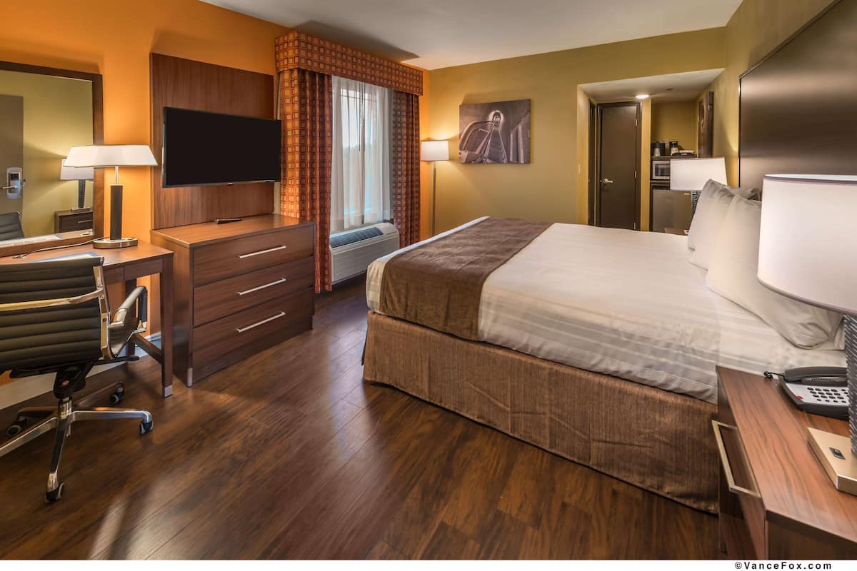 Une chambre d’hôtel avec un grand lit, un bureau avec une chaise, une télévision et une fenêtre avec des rideaux.