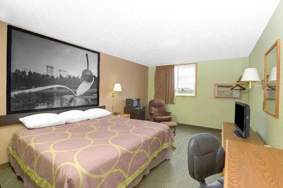 A hotel room with a bed, a desk, a chair, a television, and a large framed picture on the wall.