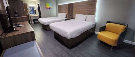 A hotel room with two beds, a desk with a computer, a chair, and a TV.