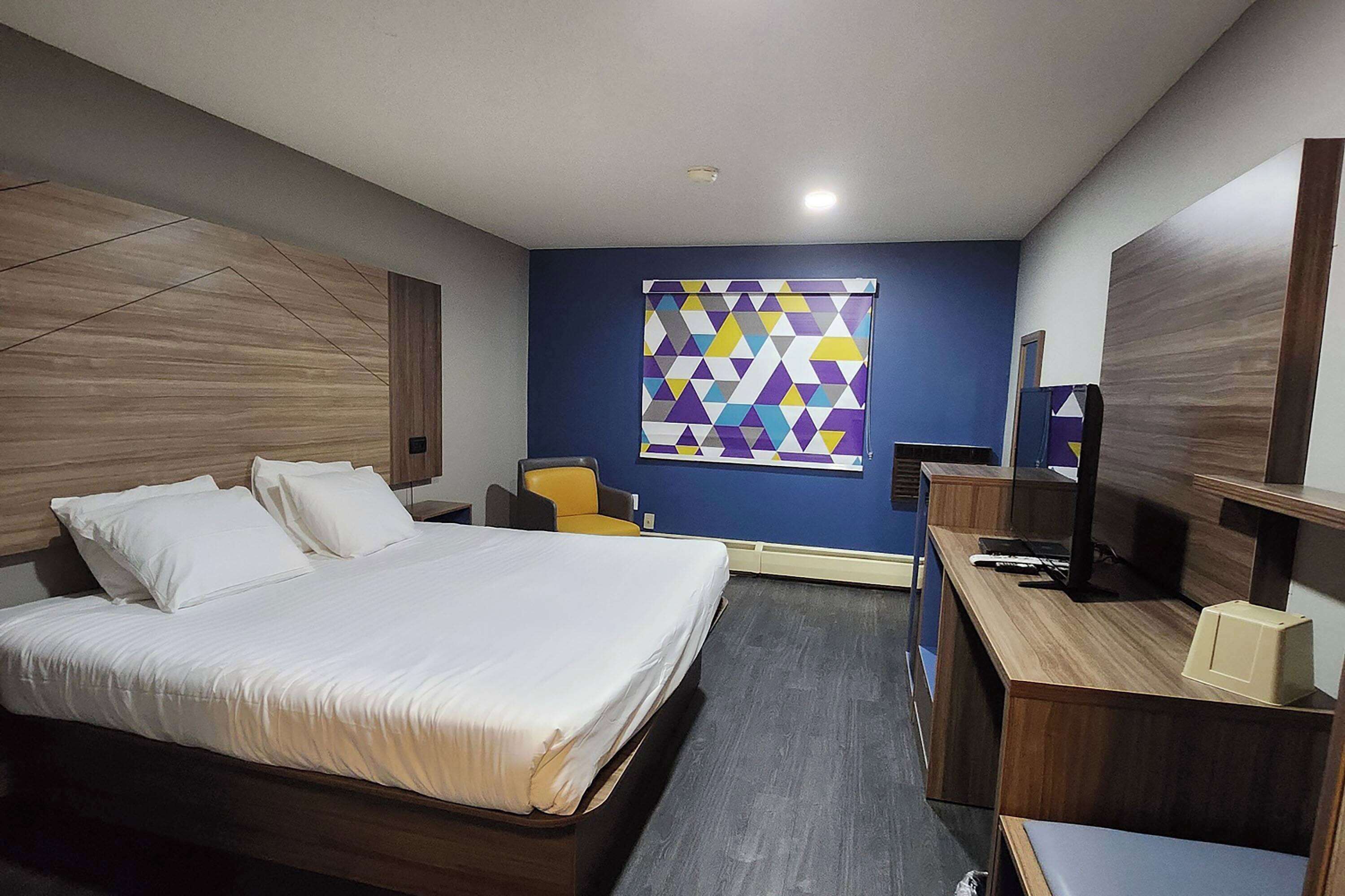 Una habitación de hotel con una cama, un escritorio, una silla y una obra de arte en la pared.