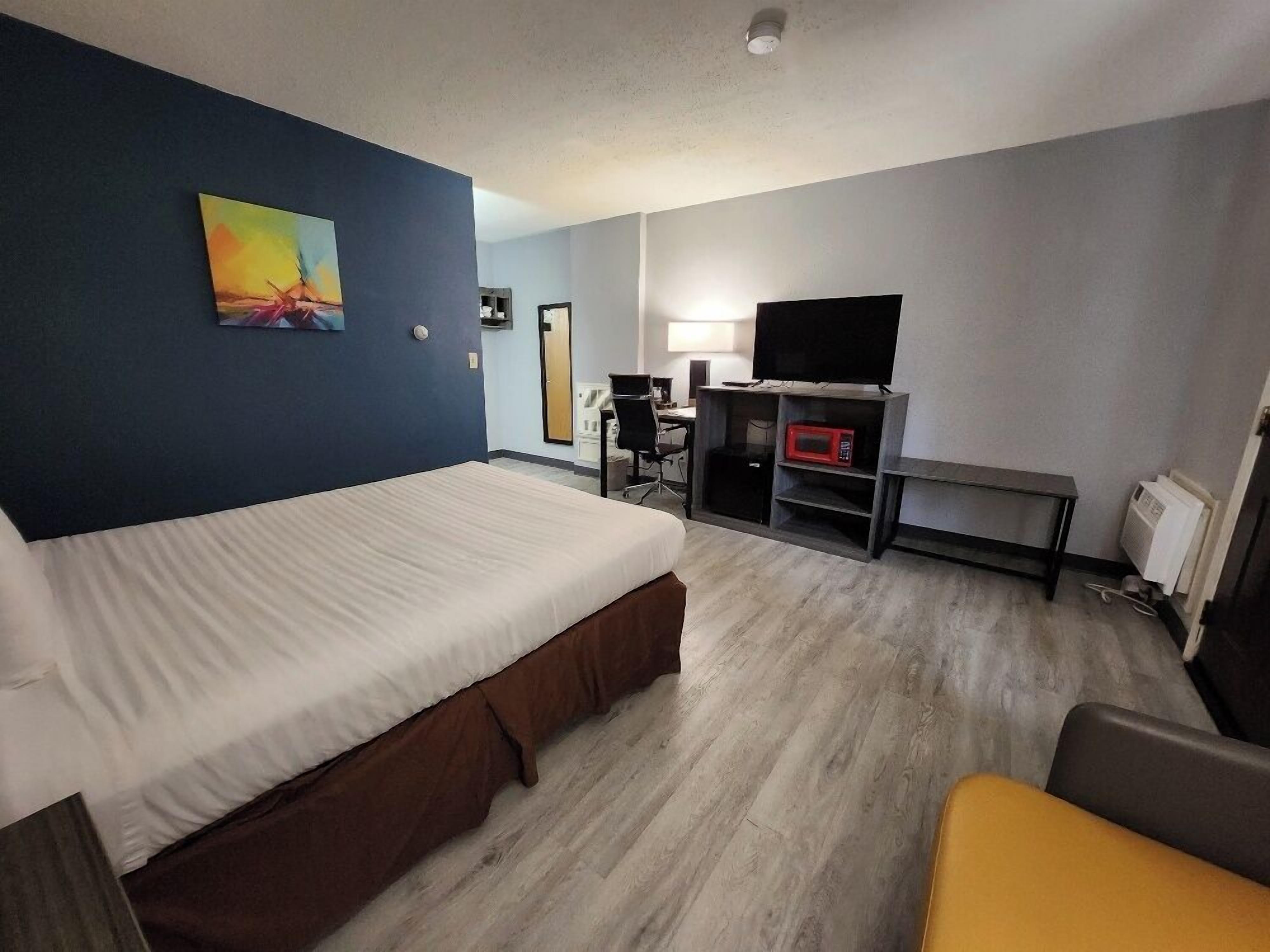 A hotel room with a bed, a desk, a chair, a TV, and a microwave.
