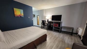 A hotel room with a bed, a desk, a chair, a TV, and a microwave.