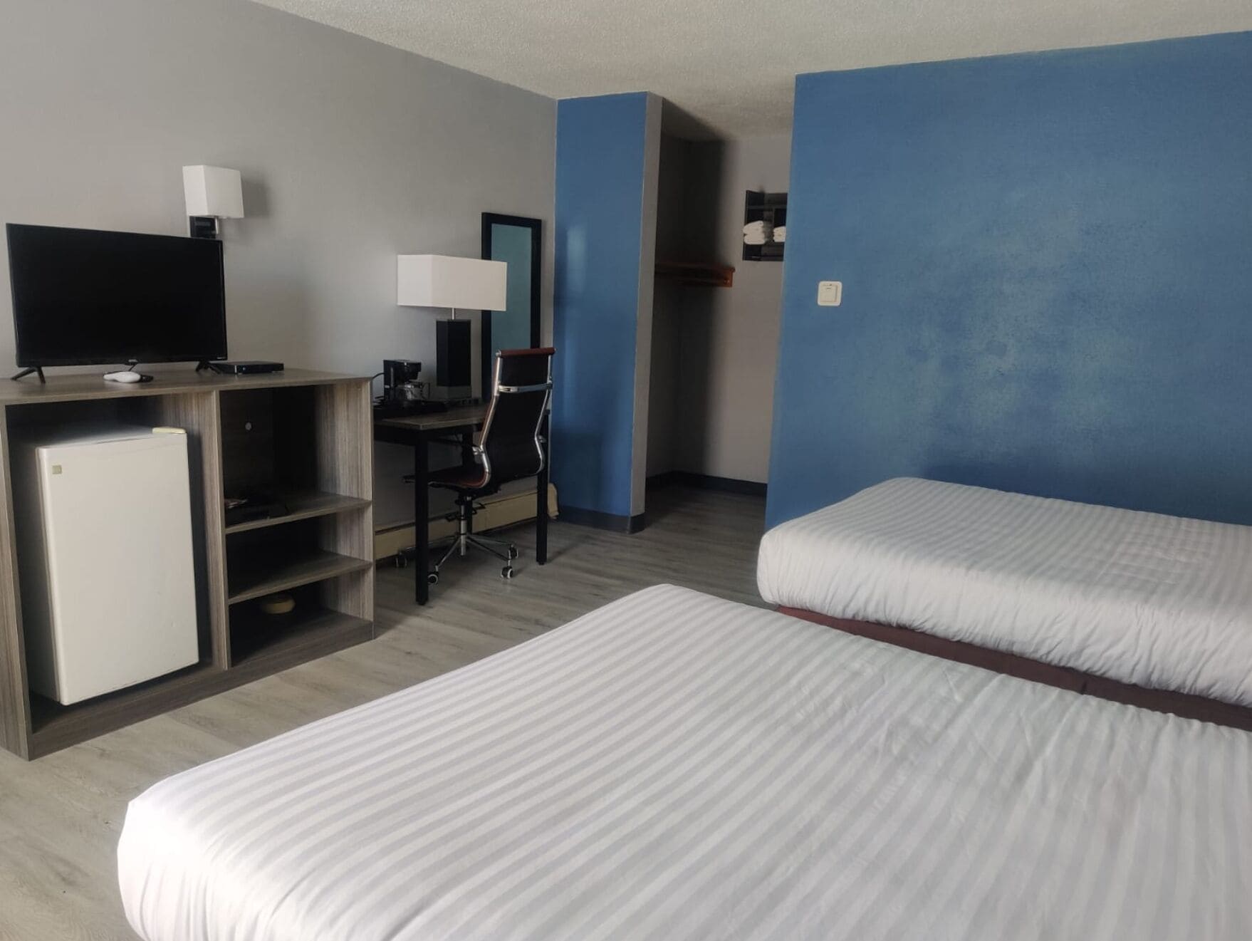 A hotel room with two beds, a desk with a computer, a TV, and a refrigerator.