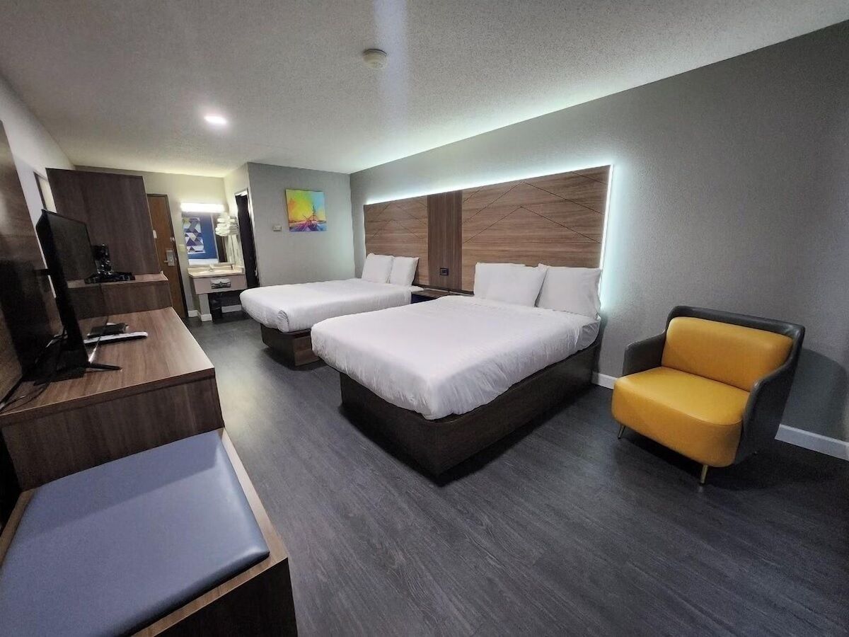 A hotel room with two beds, a desk, a chair, and a television.
