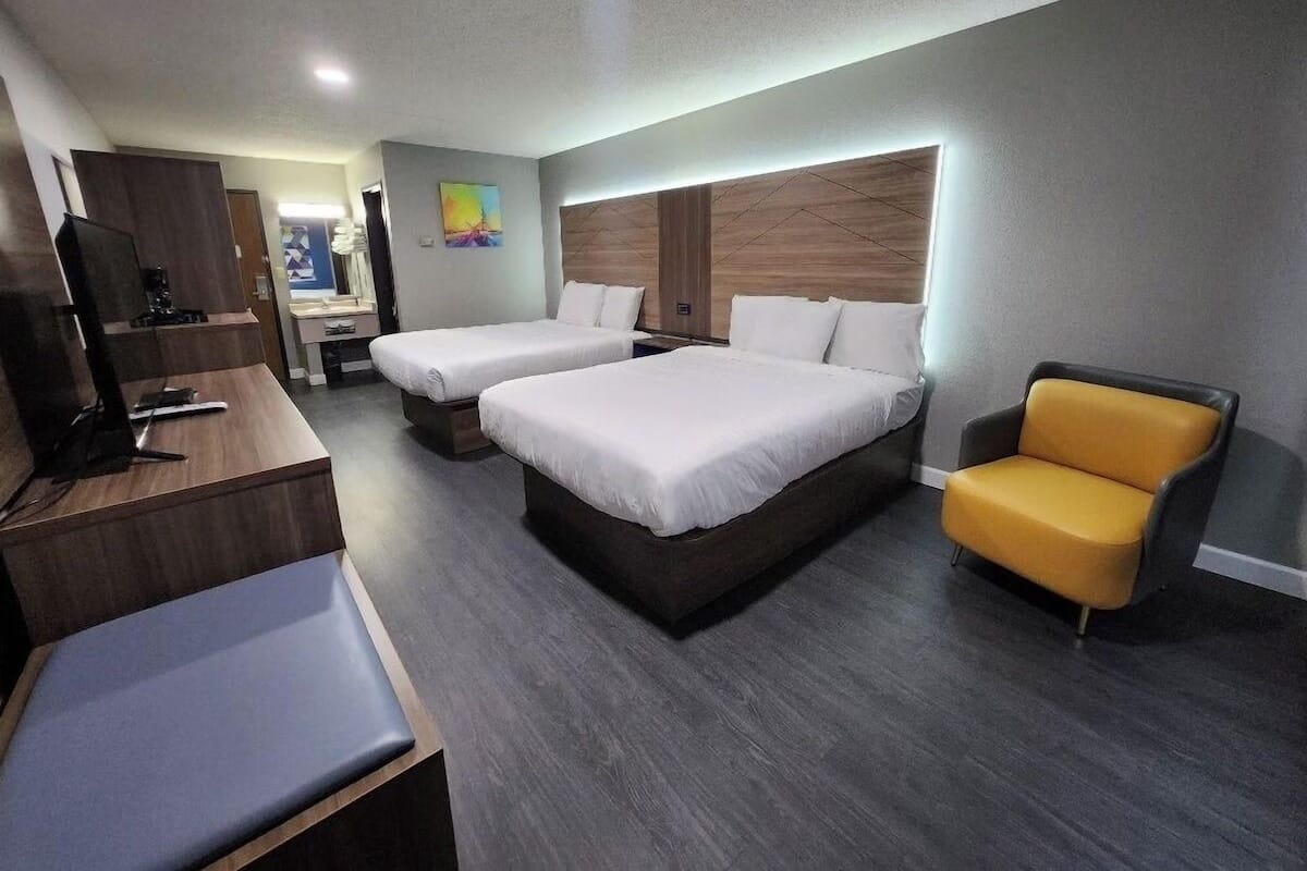 A hotel room with two beds, a desk, a chair, and a television.