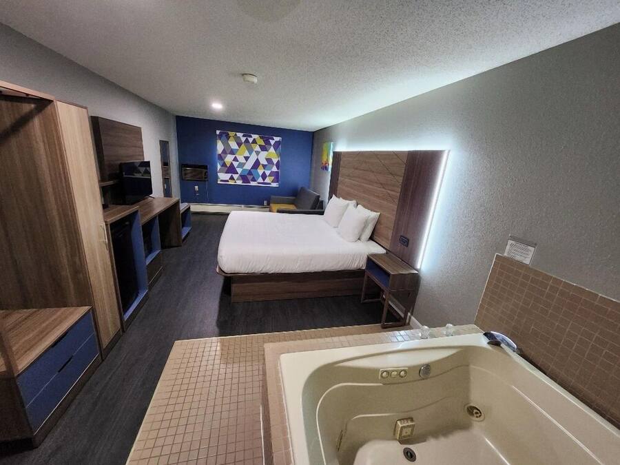 A hotel room with a large bed, a separate seating area, a small desk, a large bathtub, and a colorful geometric wall art piece.