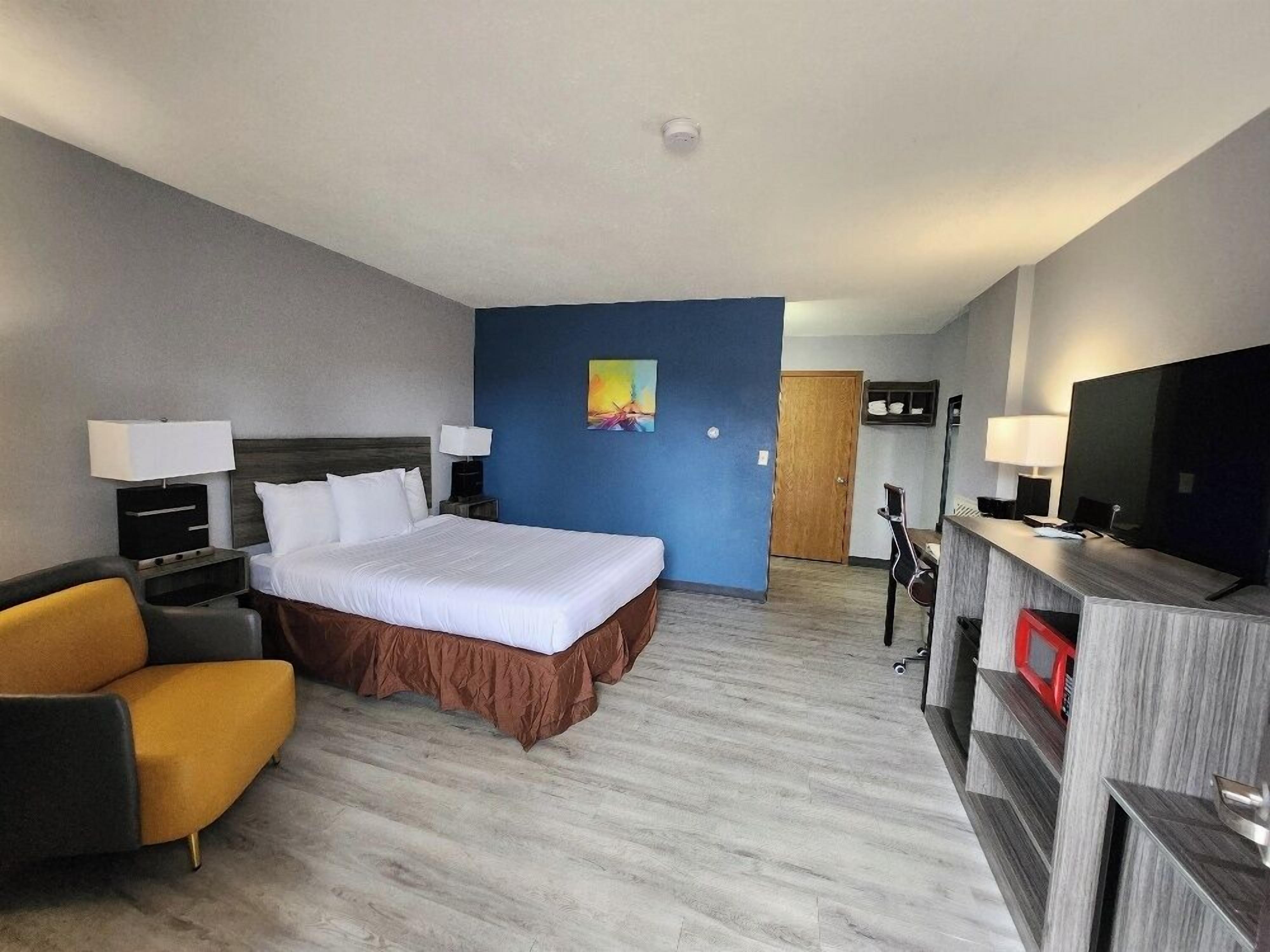 Una habitación de hotel con cama, escritorio, silla, televisor y un cuadro en la pared.