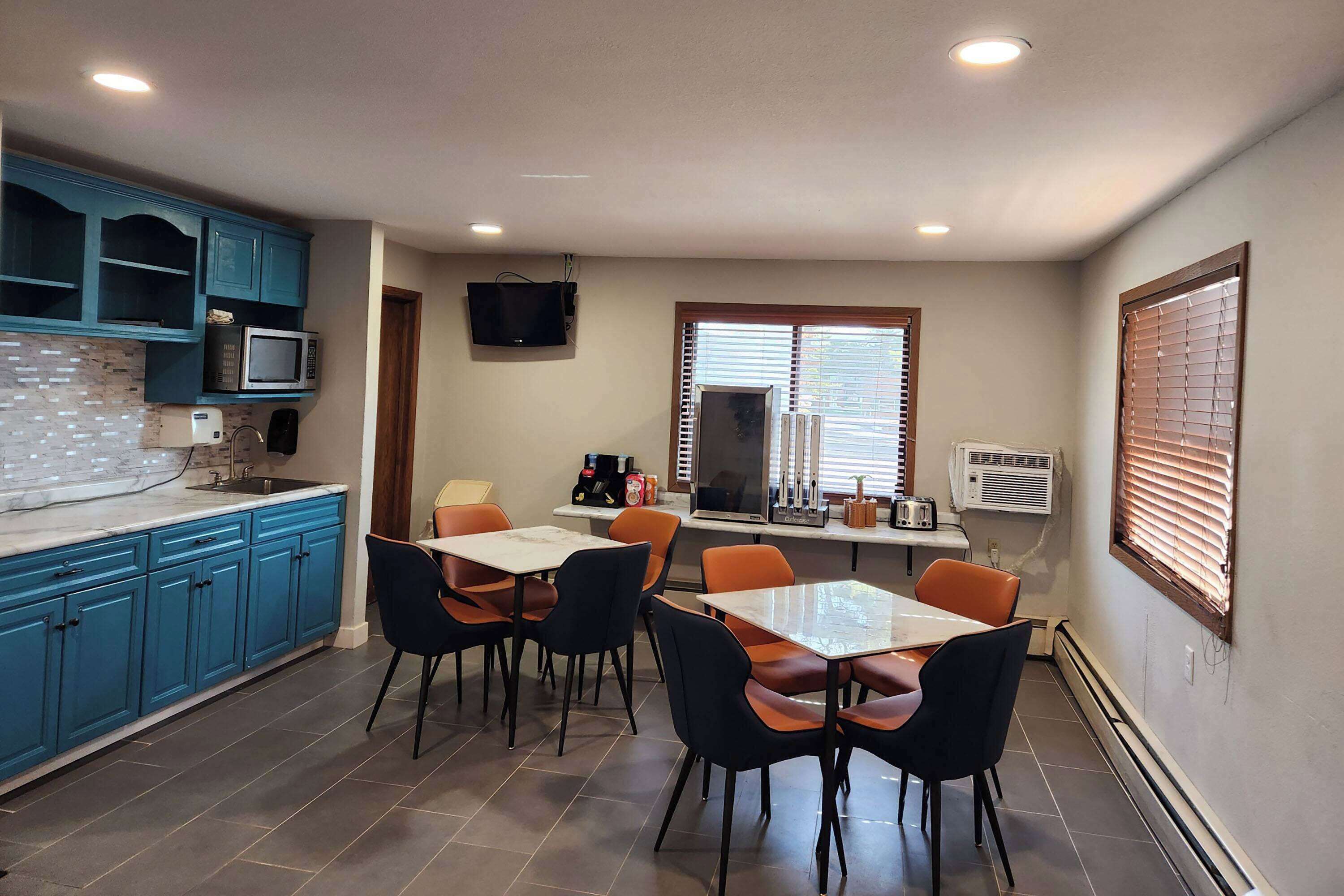 A compact kitchen with blue cabinets, a microwave, and a dining area with orange chairs.