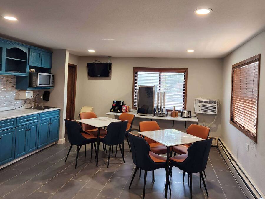 A compact kitchen with blue cabinets, a microwave, and a dining area with orange chairs.