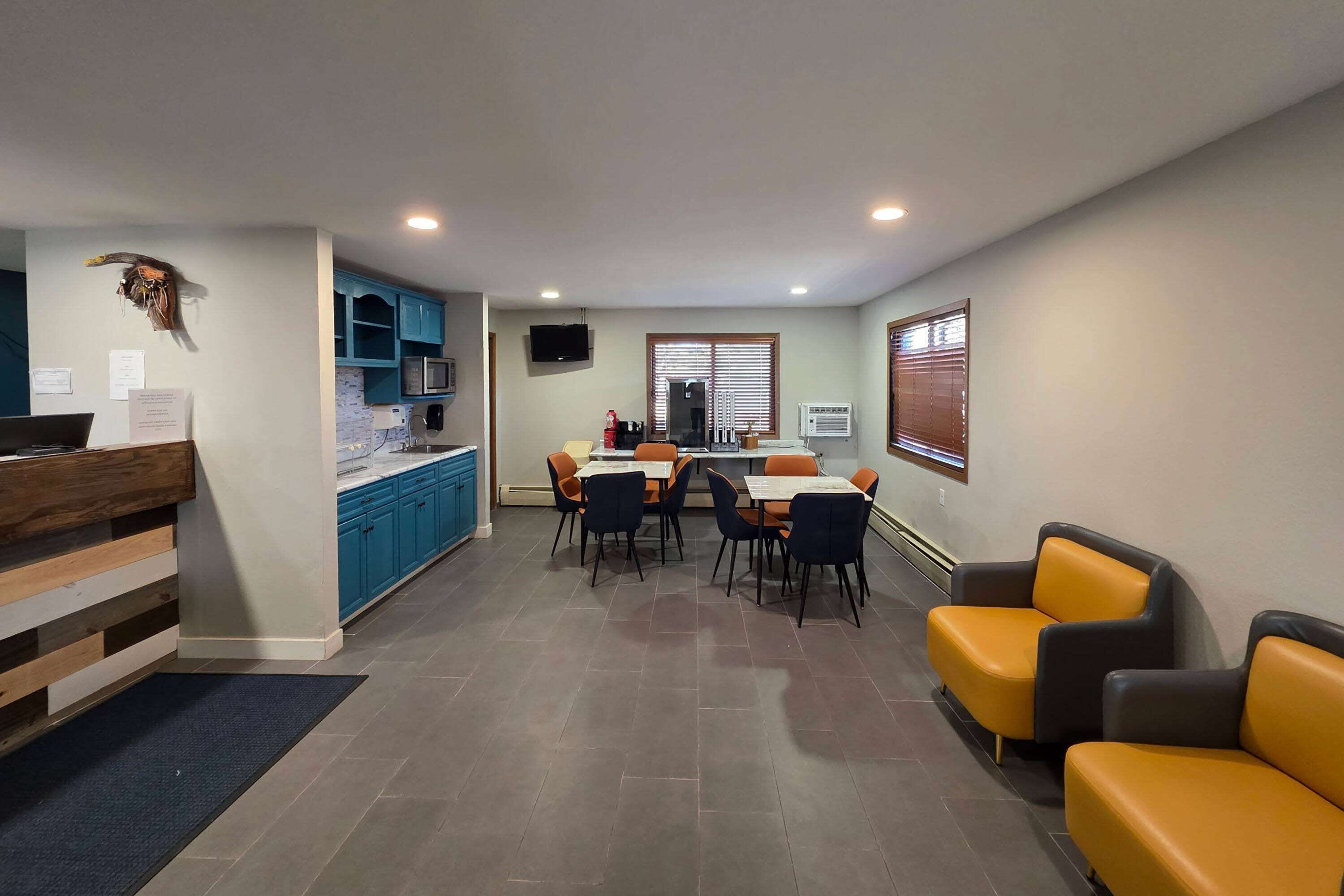Una cocina moderna con armarios azules, una zona de comedor con sillas anaranjadas y un rincón de estar con sofás amarillos y grises.