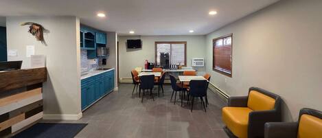 Una cocina moderna con armarios azules, una zona de comedor con sillas anaranjadas y un rincón de estar con sofás amarillos y grises.