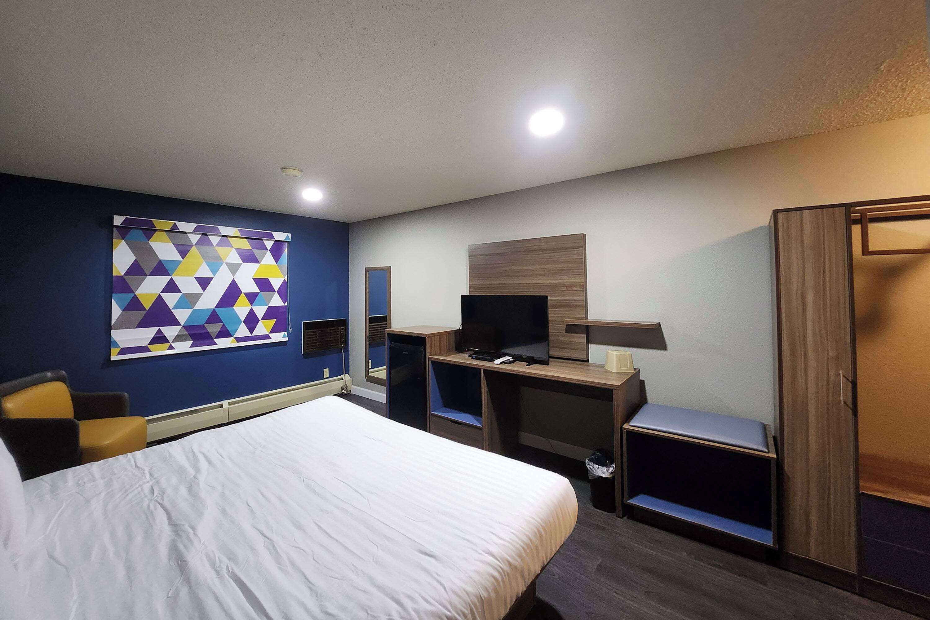 Quarto de hotel com cama, escrivaninha, televisão e guarda-roupa.