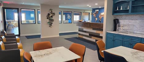 A modern hotel lobby with a reception desk, seating area, and a kitchenette.