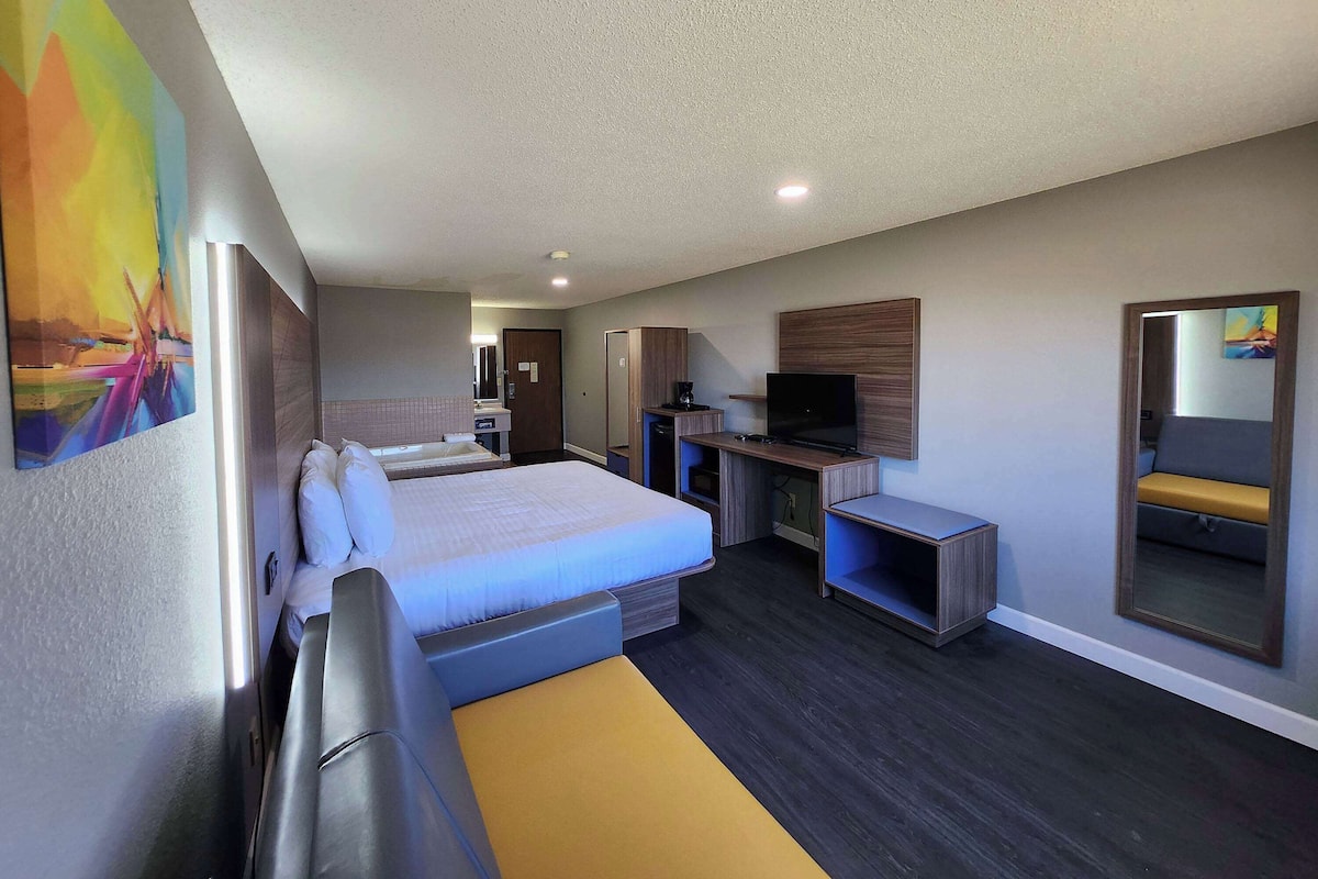 A hotel room with a bed, a desk, a chair, a television, and a mirror.