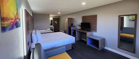 A hotel room with a bed, a desk, a chair, a television, and a mirror.