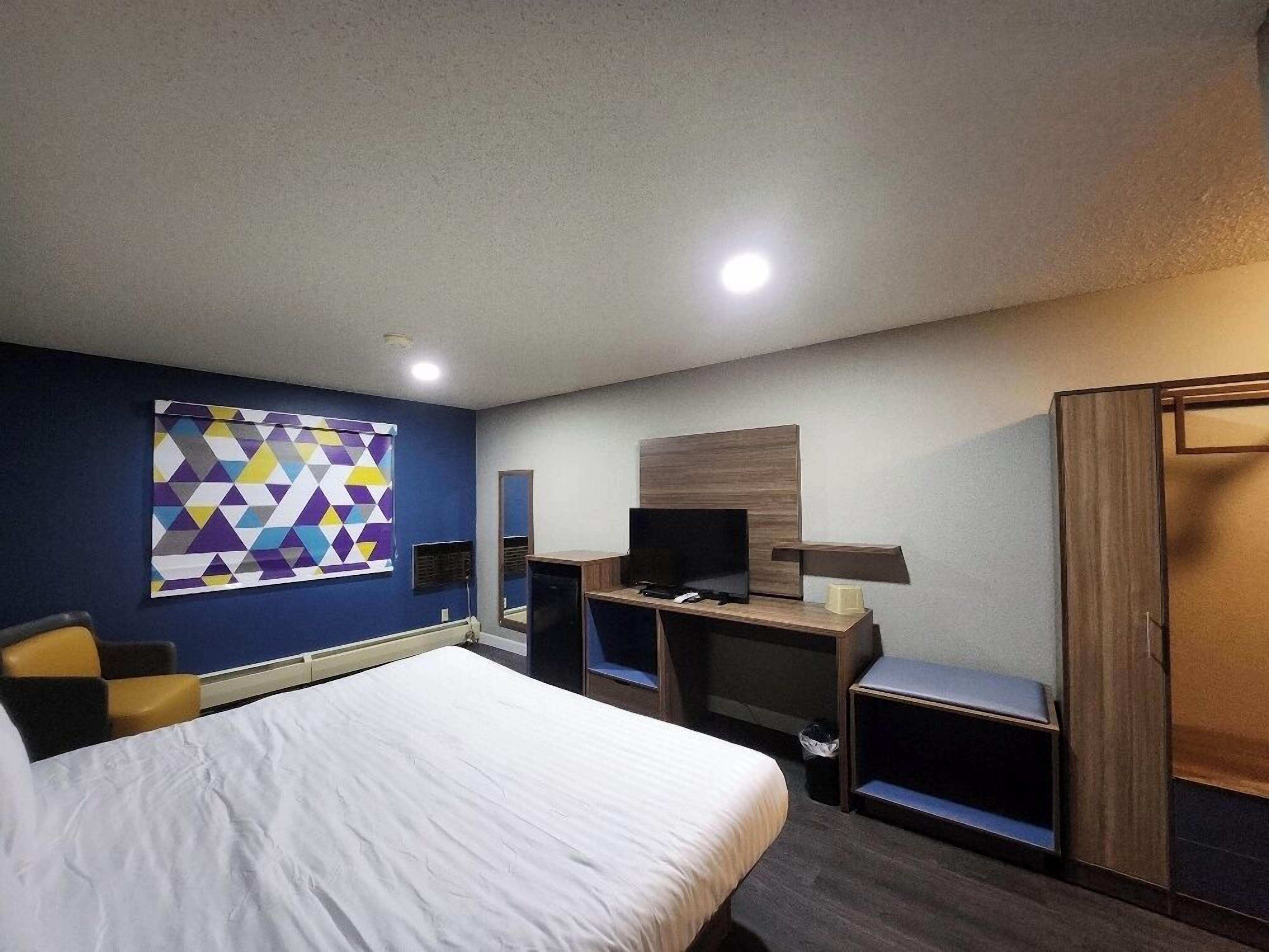 Una habitación de hotel con cama, escritorio con computadora, televisor y armario.