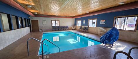 An indoor swimming pool with a wooden ceiling, tiled floor, and a covered seating area.