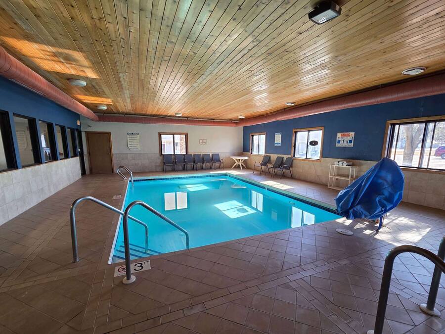 Una piscina interior con techo de madera, suelo de baldosas y una zona de estar cubierta.