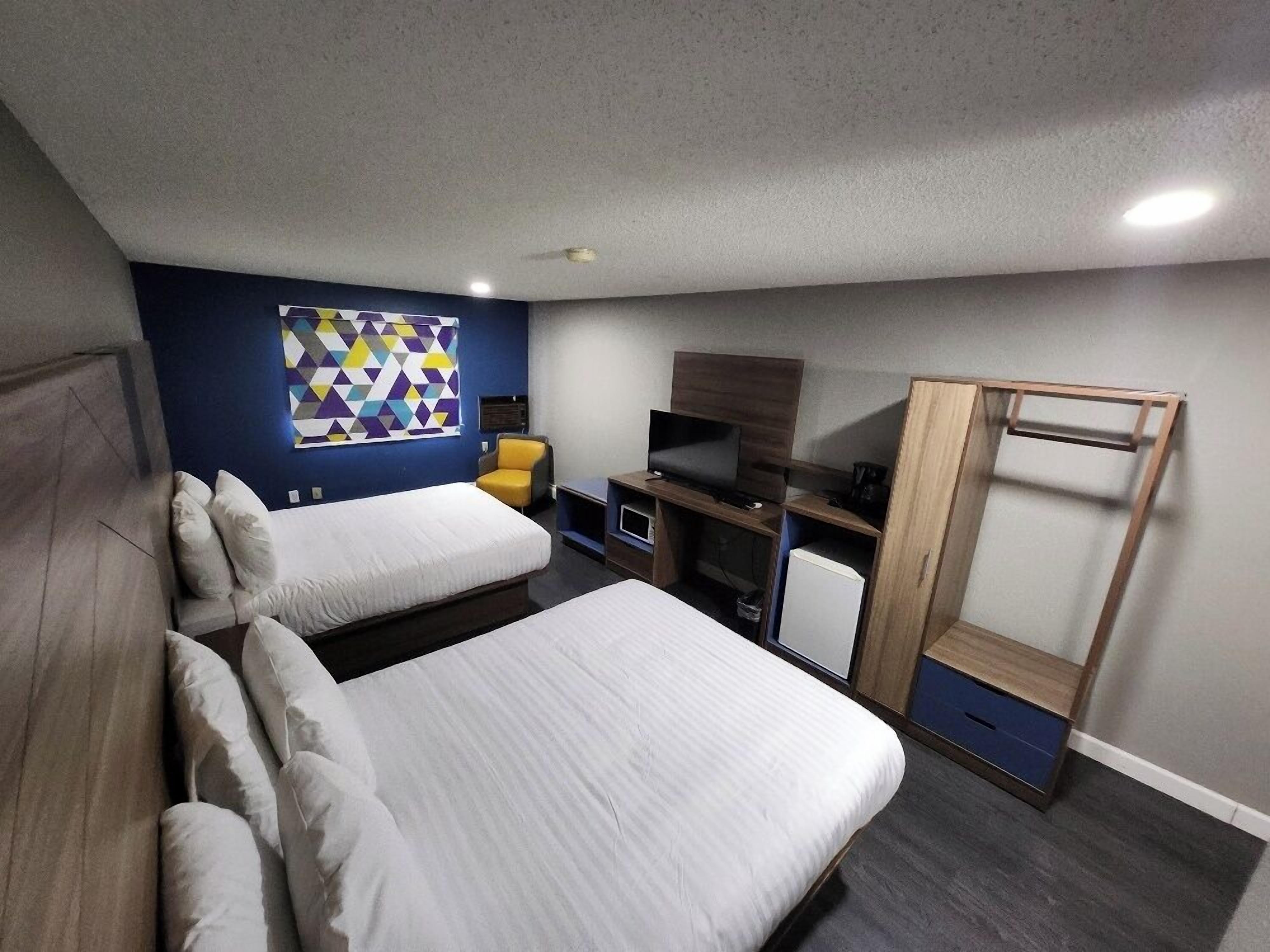 Habitació d'hotel moderna amb dos llits, televisió, escriptori i armari.