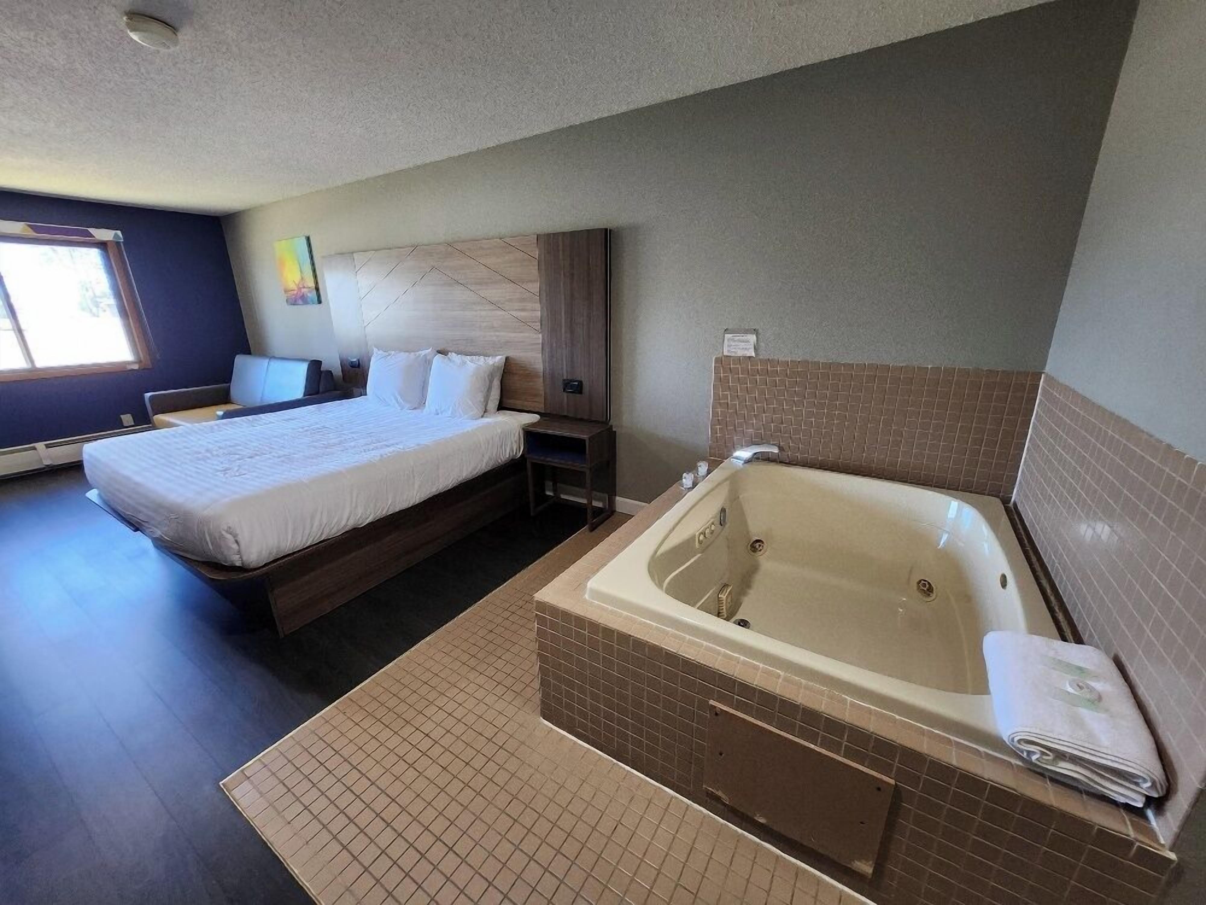 Une chambre d’hôtel dotée d’un grand lit, d’un coin salon séparé, d’une baignoire et d’une fenêtre laissant entrer la lumière naturelle.