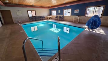 An indoor swimming pool with a wooden ceiling, tiled floor, and a pool ladder.