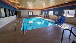 Une piscine intérieure dotée d’un sol carrelé, d’un plafond en bois et d’une fenêtre laissant entrer la lumière naturelle.